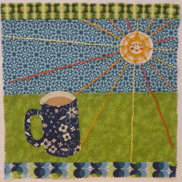 Quilt square made from patterned fabric with an embroidered sun shining down on a mug of coffee.