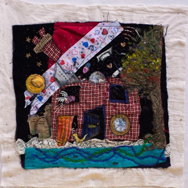 Quilt square with a house made out of different fabrics showing various items like gravestones, a graduation hat and hearts.