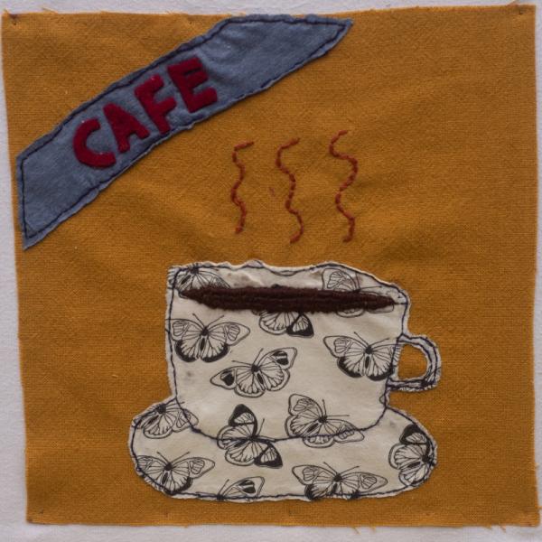 Quilt square with fabric sewn to show a CAFE banner and a cup and saucer of tea.