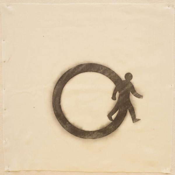 A simple symbol of a man stepping outside a circle drawn with fabric paint on a square of fabric.