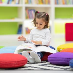 Toddler reading a book on the floor in a library
