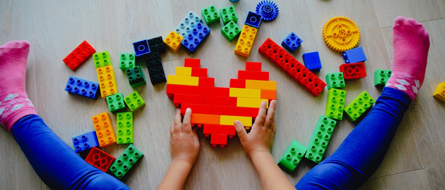 Child building a heart shape out of Lego bricks