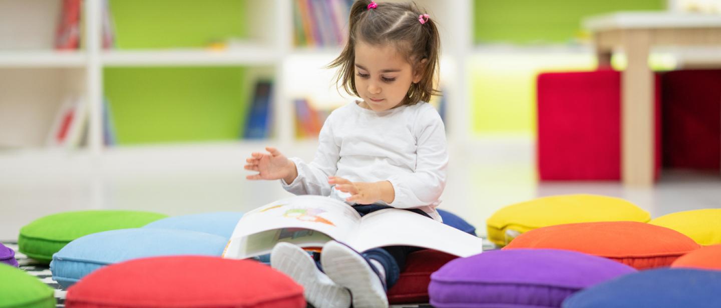 Toddler reading a book on the floor in a library