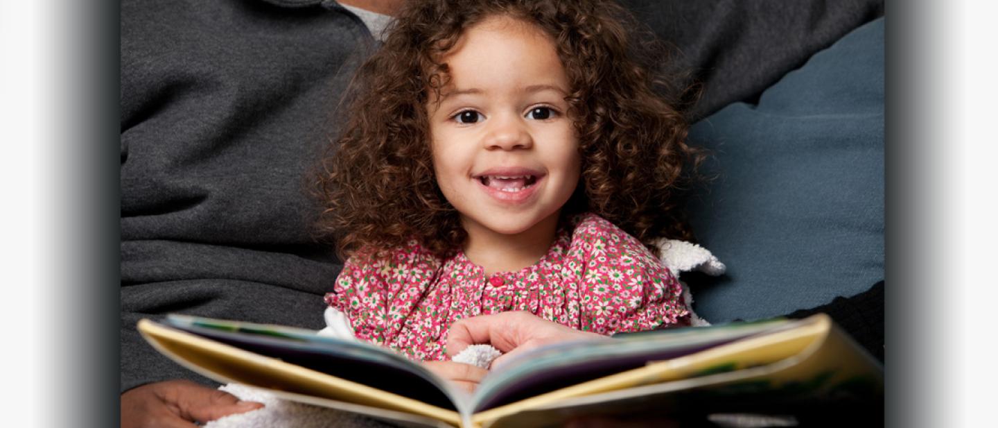 Toddler reading a book on her dad's lap