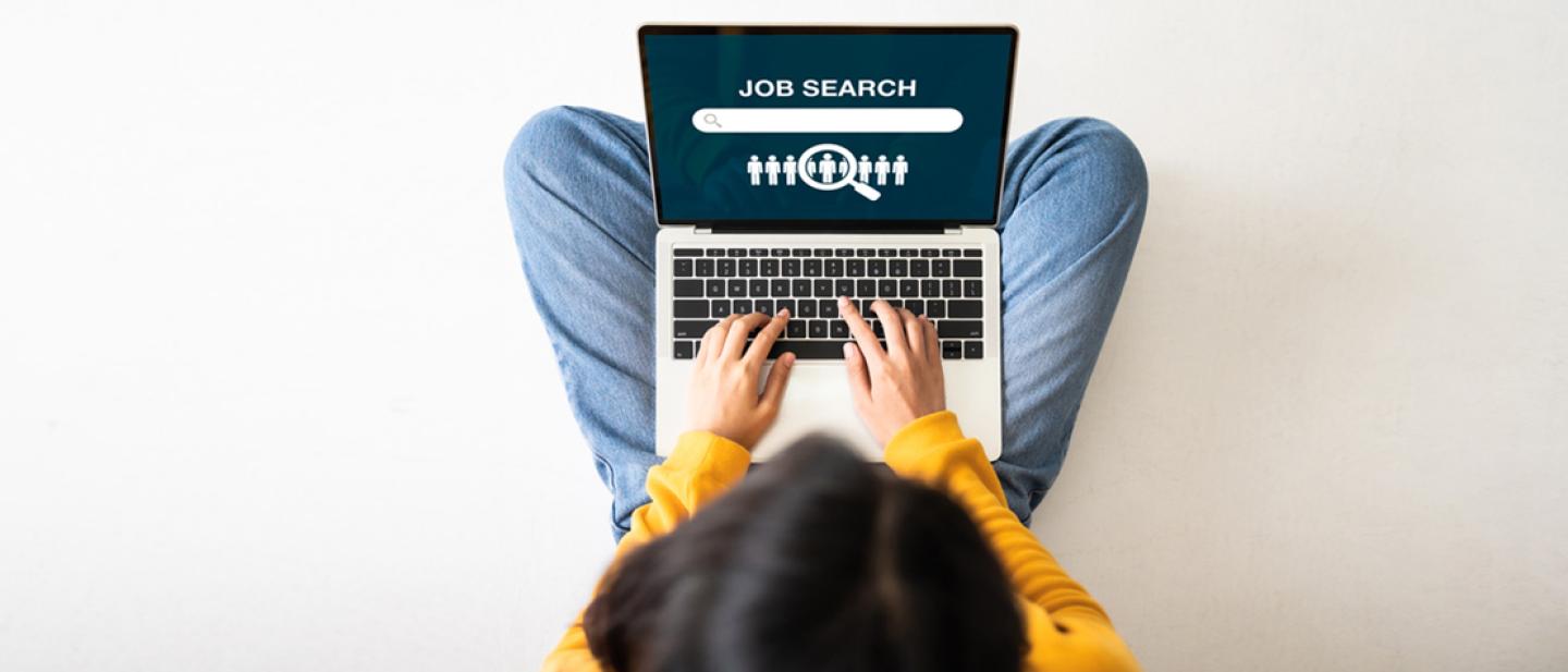 Overhead view of a girl working with a laptop balanced on her crossed legs.