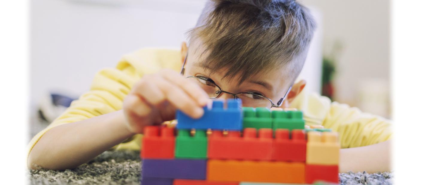 Young boy carefully building a wall with Lego bricks.