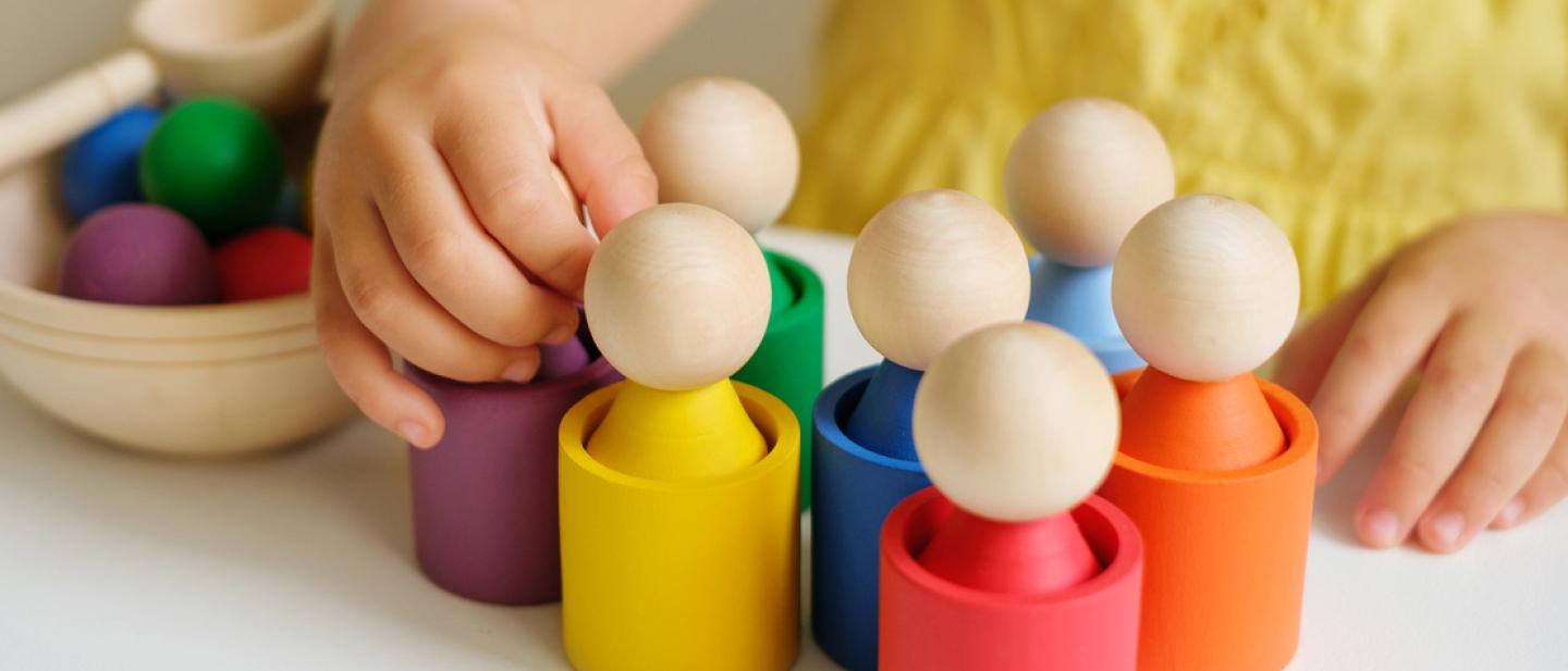 A toddler's hands shown playing with brightly coloured wooden skittles.