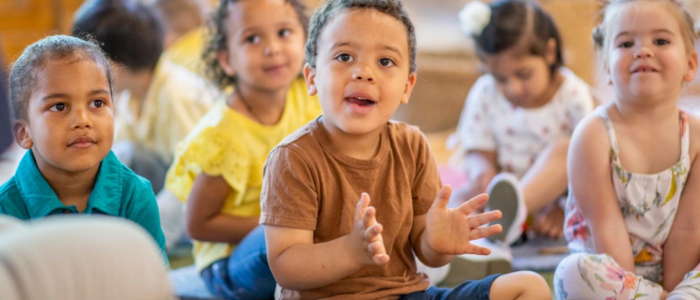 Children sitting on the floor listening to a story and smiling.