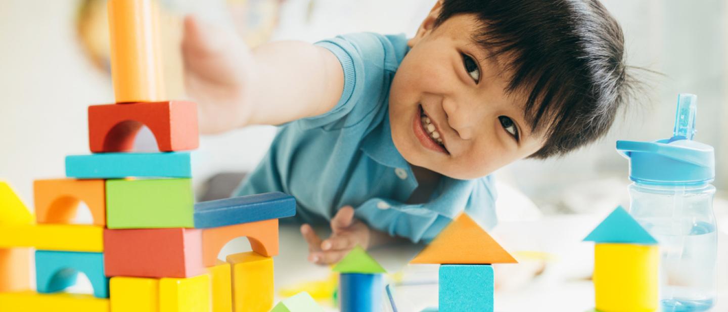 A young boy laying on the floor playing with building bricks.