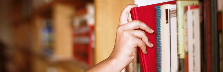 A hand choosing a book from a shelf