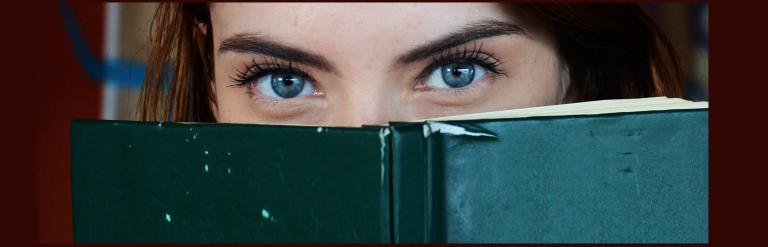 Woman's eyes peeking over the top of a book