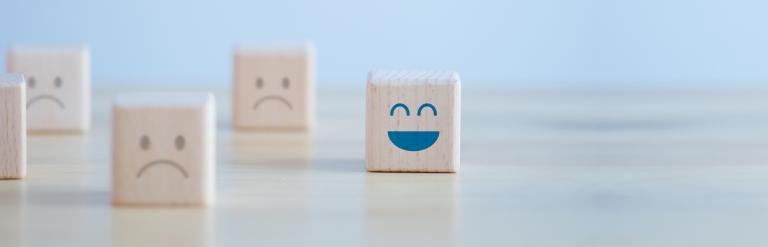 Four simple wooden cubes with different expressions on them, and the one in focus is a happy smiling face.