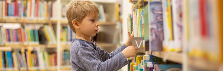 A young boy choosing a book from a shelf in a library.