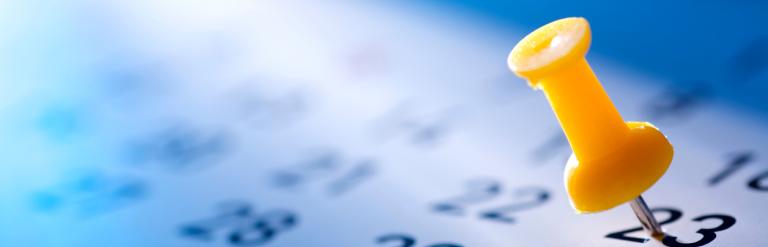 A push pin stuck on a specific date box on a calendar.