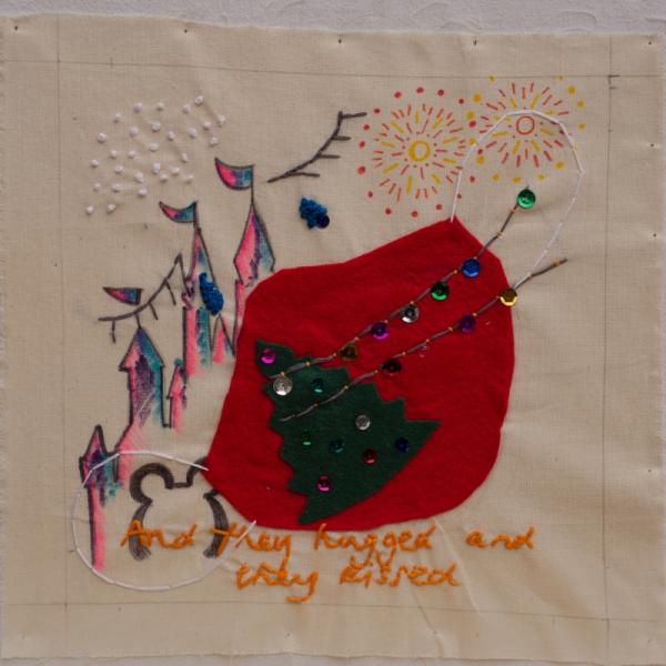 A fabric quilt square with embroidery words saying "and they hugged and they kissed" along with decorations of the Disney castle and a Christmas tree.