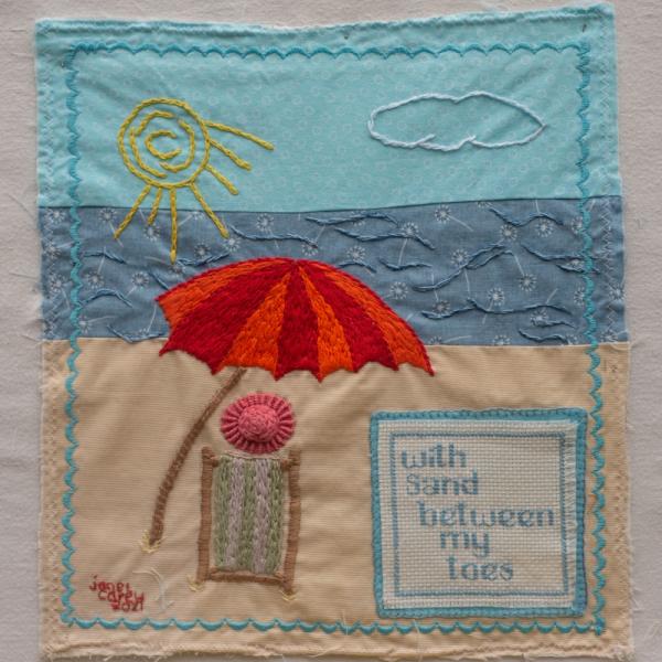 Quilt square made with fabric and embroidery showing a beach scene and the text: With Sand Between My Toes.
