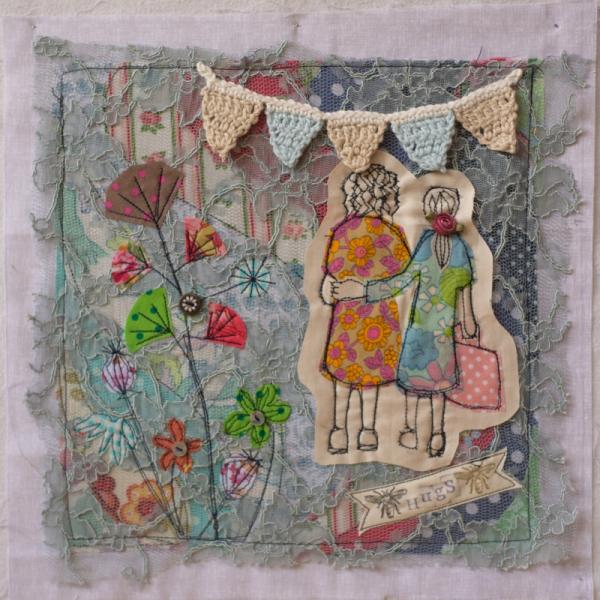 Quilt square using different printed fabric, lace and crochet to show a garden scene with bunting and two women hugging. Text reads: Hugs.