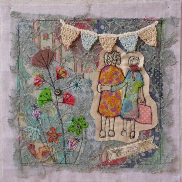 Quilt square using different printed fabric, lace and crochet to show a garden scene with bunting and two women hugging. Text reads: Hugs.
