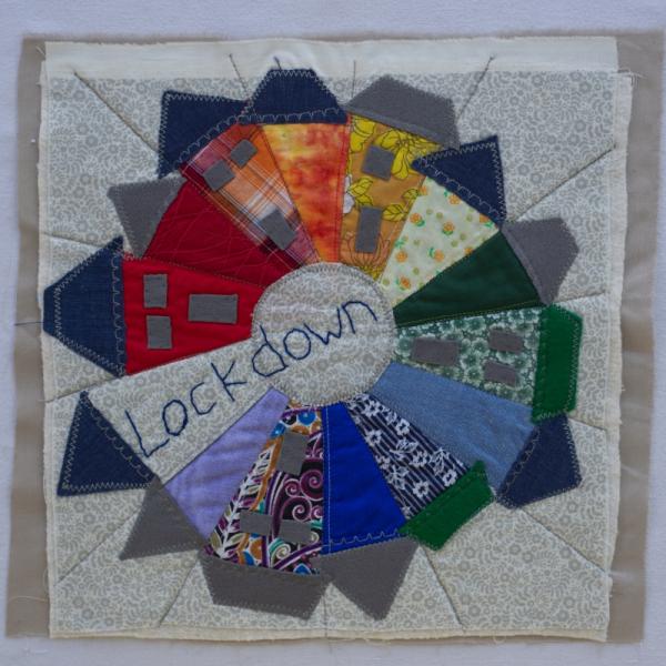 Quilt square using patterned fabric to make a circle of houses around the embroidered word: LOCKDOWN