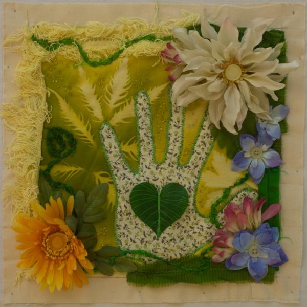 A fabric square decorated with fabric flowers surrounding a hand print sewn in the middle.