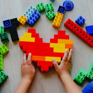 Child building a heart shape out of Lego bricks
