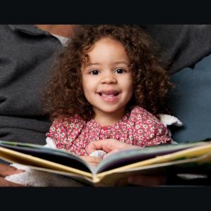 Toddler reading a book on her dad's lap