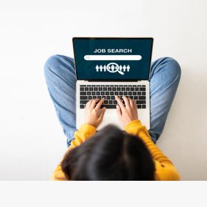 Overhead view of a girl working with a laptop balanced on her crossed legs.