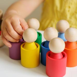 A toddler's hands shown playing with brightly coloured wooden skittles.