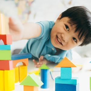 A young boy laying on the floor playing with building bricks.